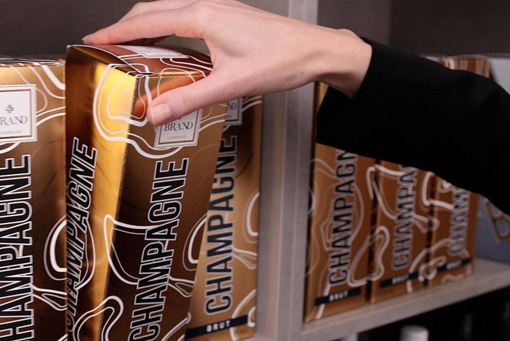 Umverpackungen & Sekundärverpackungen attraktiv & kreativ veredeln Champagnerverpackung mit Kaltfolie wird aus einem Regal genommen